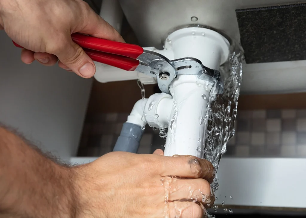 Professional plumber using adjustable wrench to repair leaking pipe under sink, demonstrating Jackson Mechanical's plumbing services in Doylestown, Bucks County.